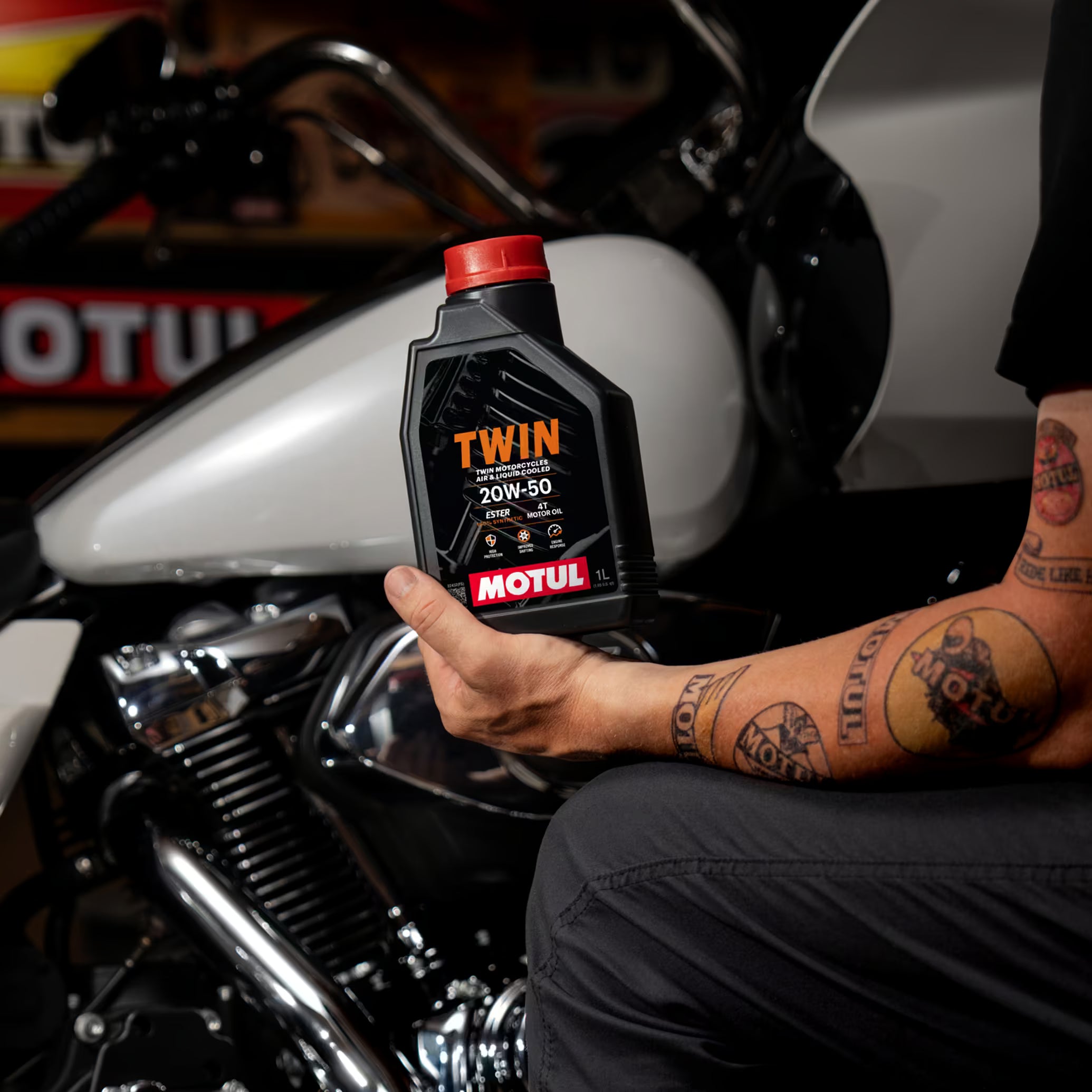 Person holding a Motul Twin oil bottle in front of a motorcycle