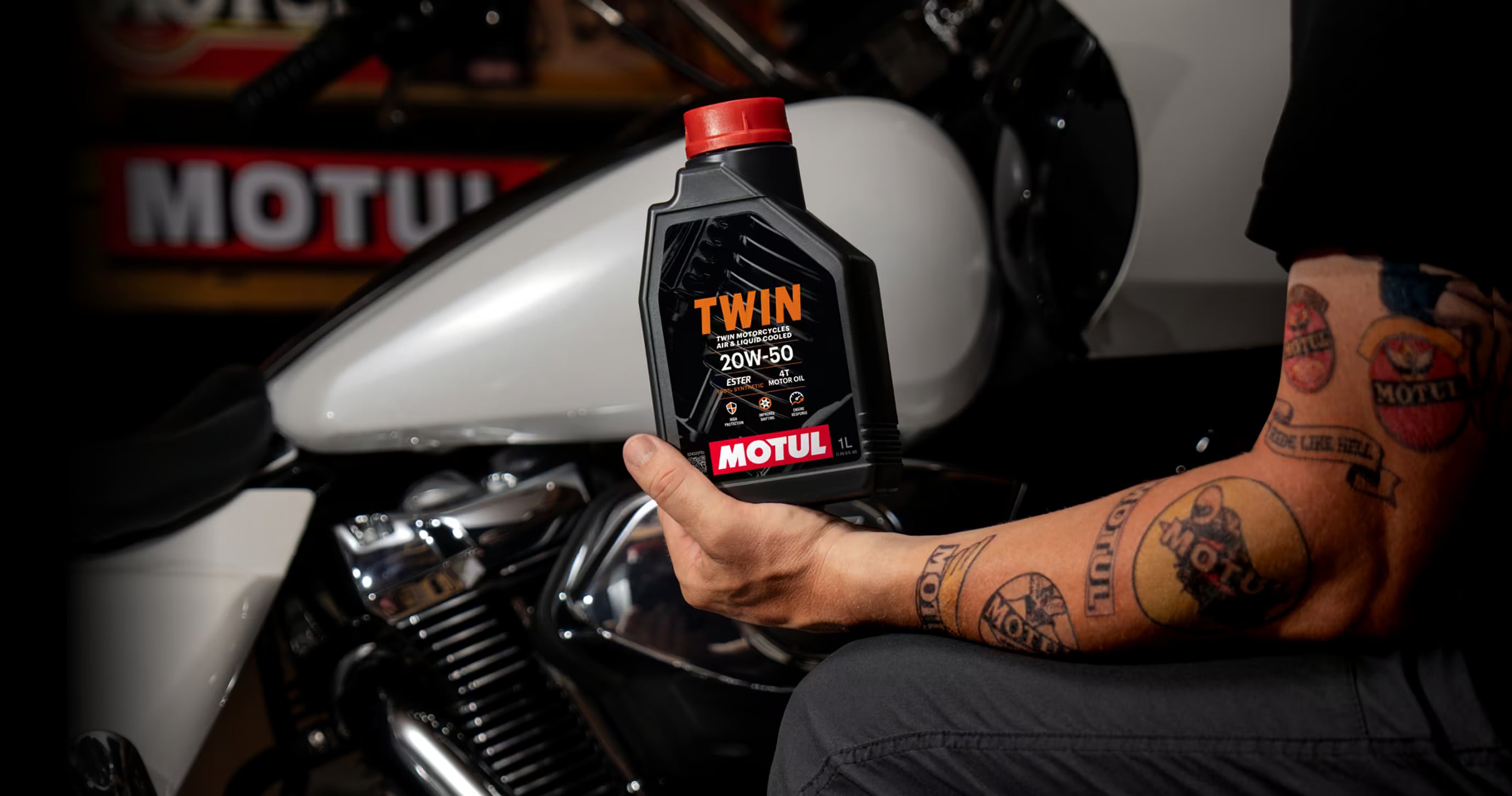 Person holding a Motul Twin oil bottle in front of a motorcycle